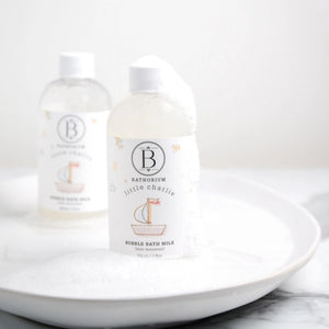 Two bottles of Bathorium Little Charlie bubble bath milk with bubbles on a white plate with a white background