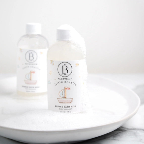 Two bottles of Bathorium Little Charlie bubble bath milk with bubbles on a white plate with a white background