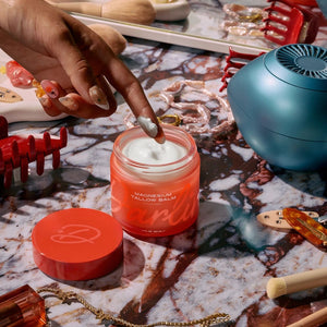 Person applying Darlin' Skincare Magnesium Tallow Balm from a jar with various items on a marble surface