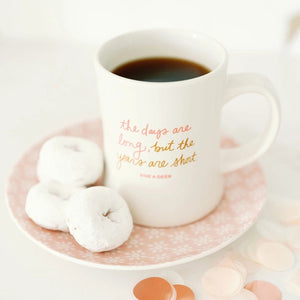 White Doe A Deer The Days Are Long Mug with text on a pink plate with doughnuts, on a white background