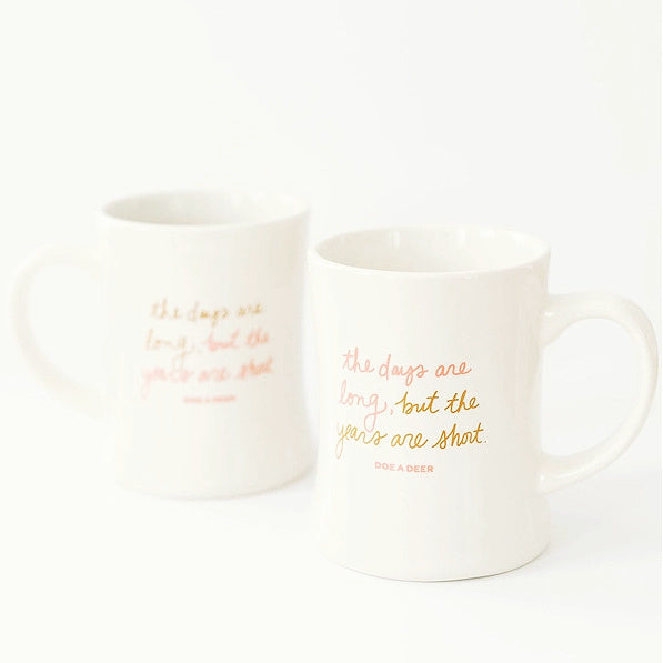 Two white The Days Are Long mugs with pink & gold text on a white background