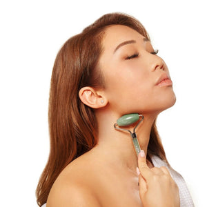 Woman using an ESW Beauty jade roller on her neck against a white background