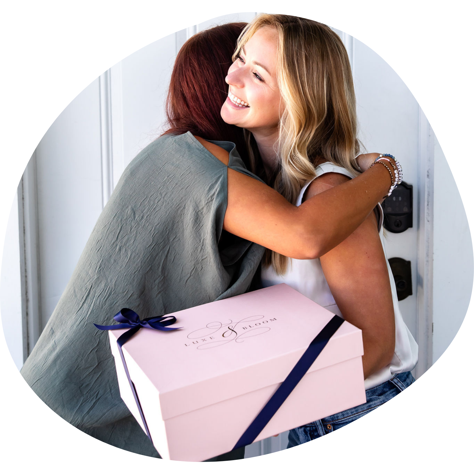 Two friends exchanging a large blush gift box and hugging.