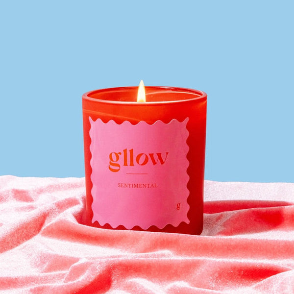 Red Gllow Sentimental candle with a pink label on a textured surface against a blue background
