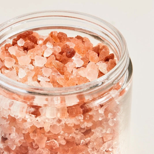 Clear glass jar filled with pink Himalayan salt on a light background