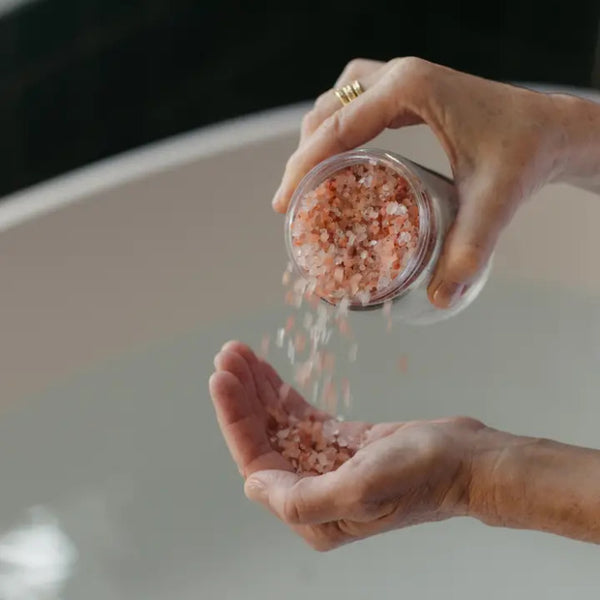 Person pouring pink Palermo Replenishing Salt Soak into their hand from a small container.