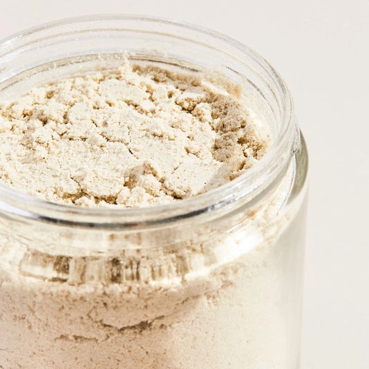 Open jar of Palermo Body Soothing Milk Bath powder on a white background