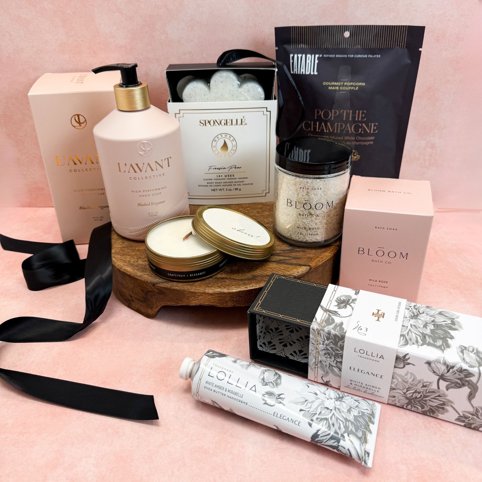 Blush & Bubbly Luxury Curated Gift Box with self care items such as L'avant Collective Blushed Bergamot Hand Soap, Lollia Ellegance Shea Butter Hand Cream, Bloom Bath Co. Wild Rose Bath Soak, Spongellé Freesia Pear Boxed Body Buffer, Cheers Tin Candle, and Pop The Champagne Popcorn 