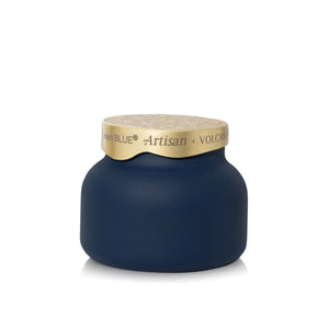 A matte navy blue jar with a textured light beige lid, featuring a gold band around the neck with the text 'capri BLUE Artisan VOLCANO'.