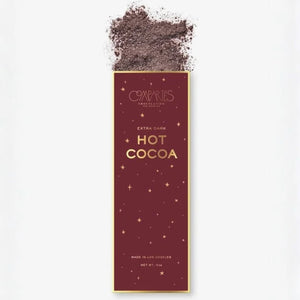 A tall rectangular package of Compartés Chocolate Extra Dark Hot Cocoa, featuring a deep burgundy background with gold text and star details, with cocoa powder spilled at the top against a white background.