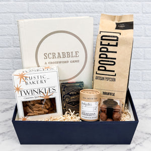 Game Night Luxury Curated Gift Box from Luxe & Bloom with Bookshelf Edition Scrabble board game, Monarch Playing Cards, Popped Truffle Artisan Popcorn, Rustic Bakery Cinnamon Spice Twinkle Cookies, Tea with Tae Bombay Chai, and Sugarfina Espresso Martini Truffles in a navy gift box