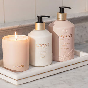 L'AVANT Collective products including a candle and bottles of lotion and hand soap on a marble surface.