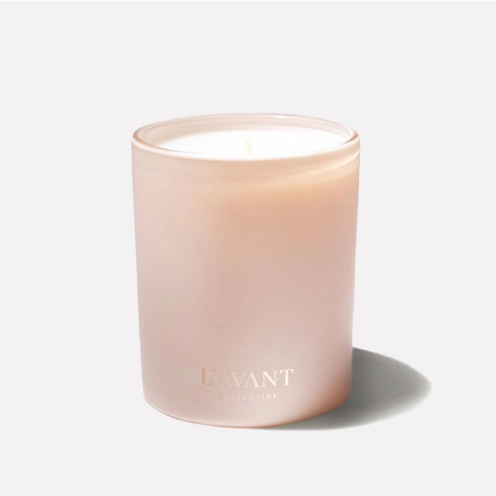 A Blushed Bergamot frosted glass jar candle with a single wick, featuring a soft blush pink color and gold foil branding that reads 'L'AVANT COLLECTIVE'. The candle is set against a solid off-white background with a soft shadow cast to the right.
