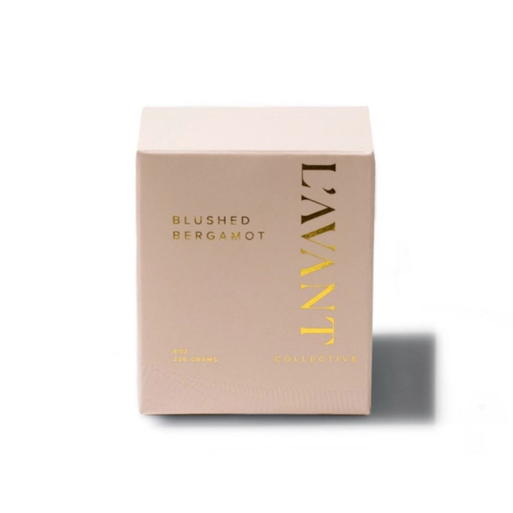 A Blushed Bergamot frosted glass jar candle with a single wick, featuring a soft blush pink color and gold foil branding that reads 'L'AVANT COLLECTIVE'. The candle is set against a solid off-white background with a soft shadow cast to the right.