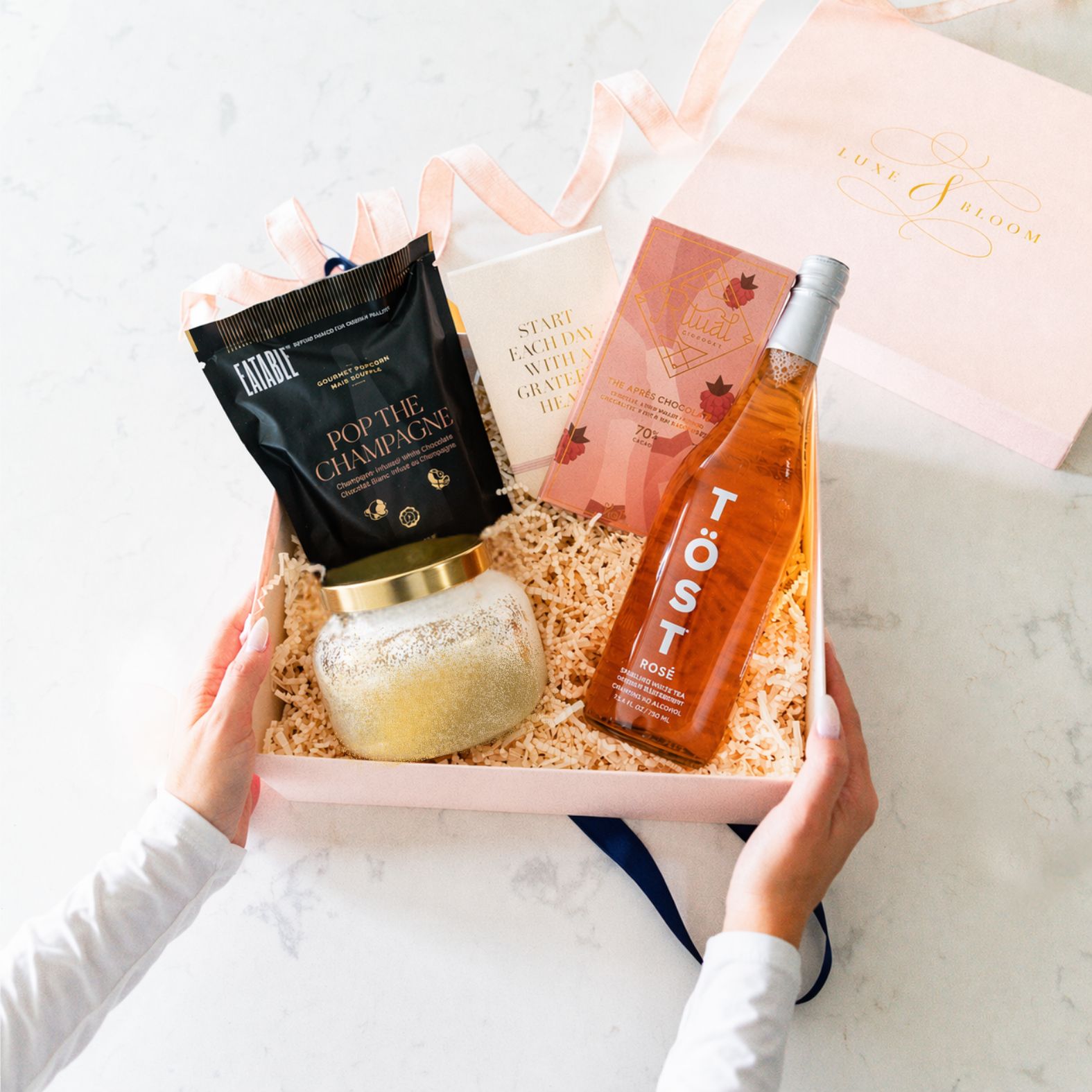 Woman holding Let's Toast Luxury Curated Gift Box For Women from Luxe & Bloom on a marble countertop