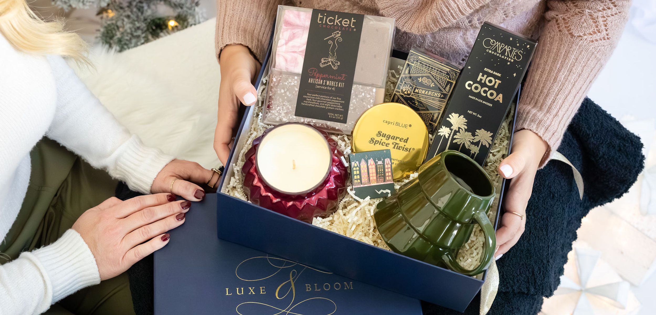 Woman holding Fireside Luxury Curated Gift Box including candles, hot chocolate, Christmas tree mug, s'mores kit, and other gift items. Luxury Curated & Custom Christmas Gift Boxes from Luxe & Bloom