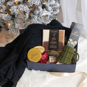 Fireside Luxury Curated Christmas Gift Box with candle, hot cocoa, mug, blanket, and more in front of a Christmas tree