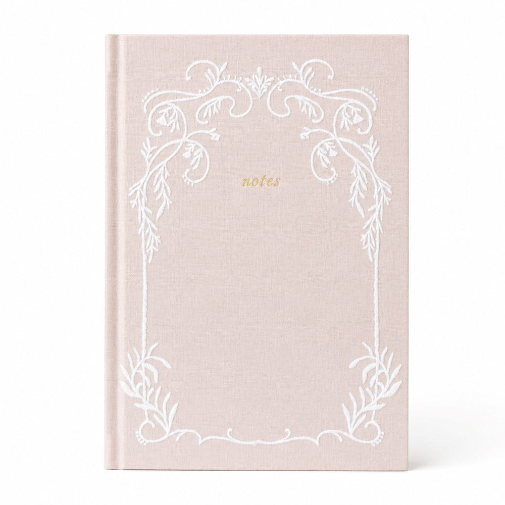 Selah Publications The Lainey Notebook: A linen colored hardcover notebook with a white ornate stitched floral border and the word 'notes' in small gold script near the upper center, shown on a clean white background.