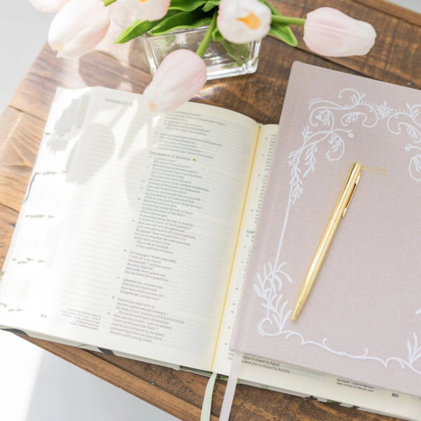 Open Bible with a Selah Publications Lainey Notebook and pink tulips and a pen on a wooden surface