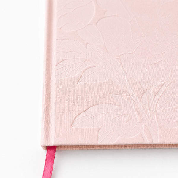 A close-up of Selah Publications The Polly Blair Notebook with light pink hardcover notebook or journal with an embossed floral pattern on the cover and a bright pink ribbon bookmark visible along the left edge, set against a plain white background.