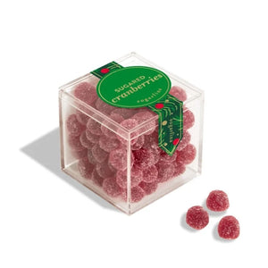 A Sugarfina clear square acrylic box filled with round, sugar-coated red cranberry candies, with a green circular label reading 'SUGARED cranberries' and three loose candies placed in front on a white background.