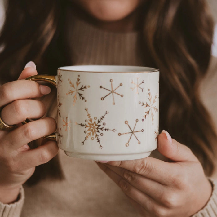 Woman holding a mug with gold snowflake patterns against a blurred background