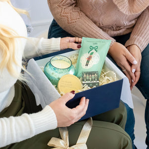 Woman holding The Nutcracker Luxury Curated Christmas Gift Box with Capri Blue Volcano candle, Latika Nutcracker bath soak, and One & Only Paper Nutcracker Matchbook