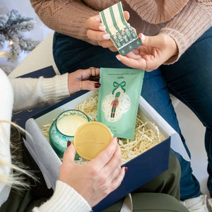 Woman holding The Nutcracker Luxury Curated Christmas Gift Box with Capri Blue Volcano candle, Latika Nutcracker bath soak, and One & Only Paper Nutcracker Matchbook
