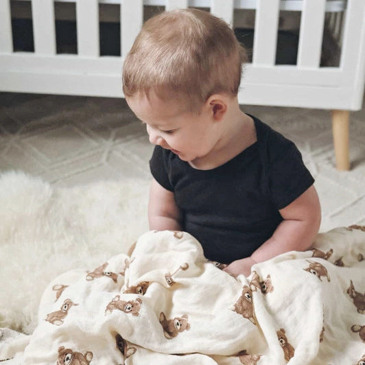 Child playing with a Ali + Oli Bamboo Muslin Teddy Bear Swaddle Blanket in a home setting.