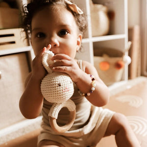 Child holding a crochet bunny toy with wooden ring in a cozy indoor setting