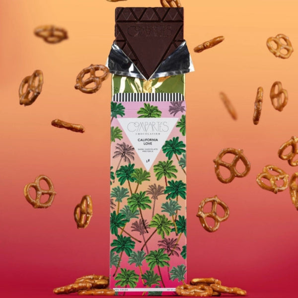 Package of Compartés Chocolate California Love Chocolate bar with pretzels all around it on an orange and pink background | Build a luxury custom gift box for women with Luxe & Bloom