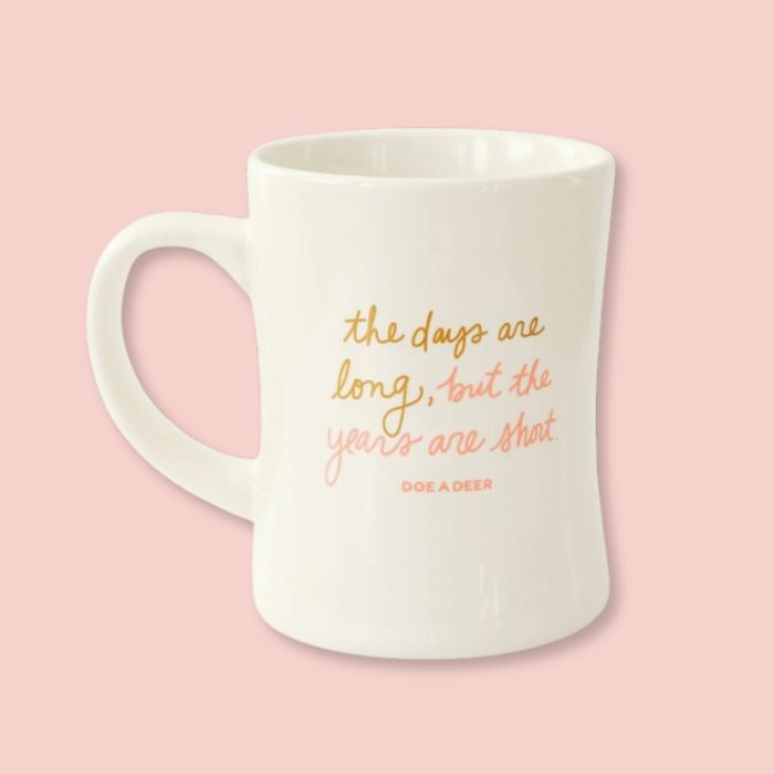 White Doe A Deer The Days Are Long Mug with text on a pink plate with doughnuts, on a white background