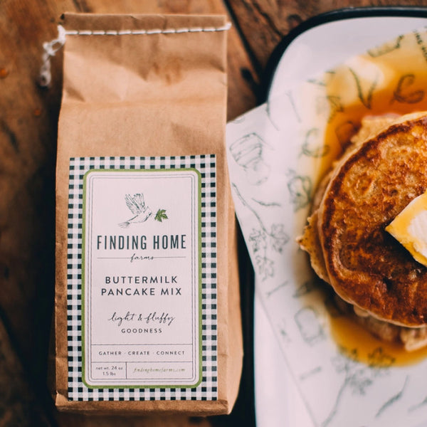 Bag of Finding Home Farms Buttermilk Pancake Mix next to a plate of pancakes with syrup and butter.