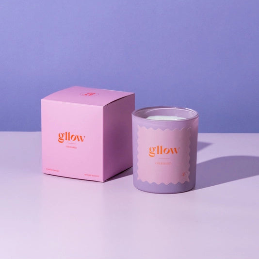 Gllow Cherished Scented Candle on a decorative stand with lemons and oranges against a purple background | Build A Luxury Custom Gift Box for Women with Luxe & Bloom