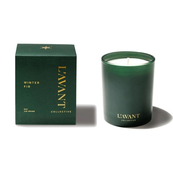 A dark green glass jar candle next to its matching dark green box packaging, both featuring gold lettering for the brand 'L'AVANT COLLECTIVE' and the scent name 'WINTER FIR'.
