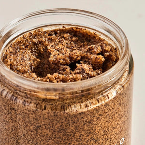 Close-up of a jar filled with brown coffee scrub on a neutral background