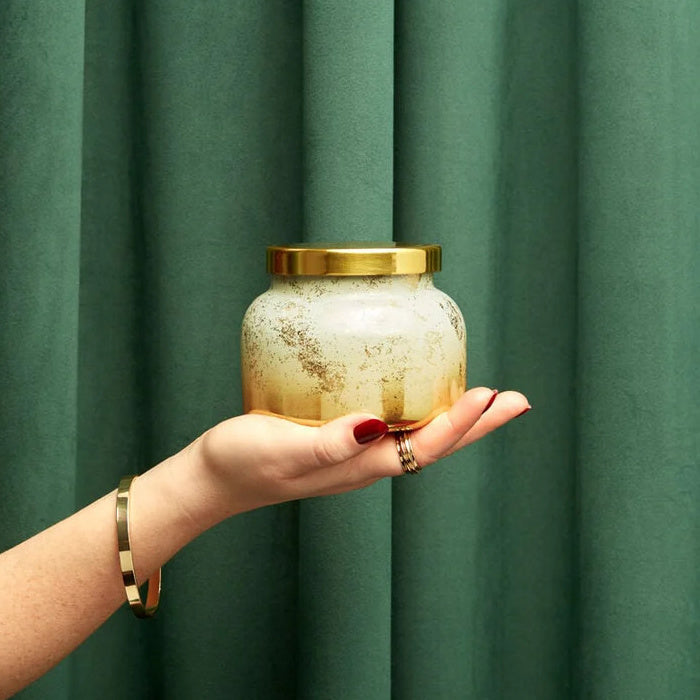 Woman Holding a Volcano Glimmer Jar Candle 19 oz with a green background